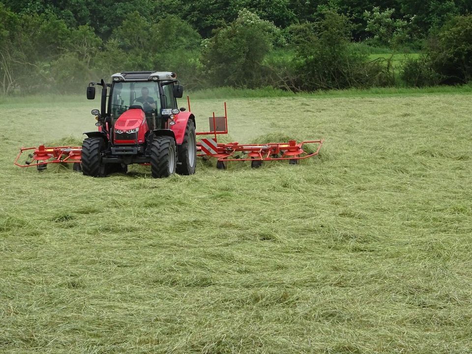 Traktor mit Heuwender auf einer gemähten Wiese