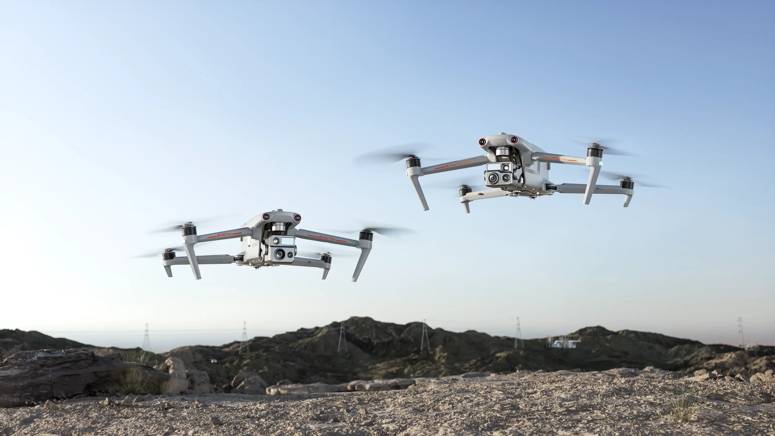 Zwei Autel EVO Max im Flug über einer Hügellandschaft mit Hochspannungsmasten